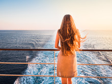 Stylish, Beautiful Woman On An Empty Deck Of A Cruise Ship Against A Background Of Sea Waves, Blue Sky And Sunset