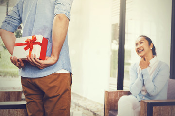 Wall Mural - Teenage son hiding a surprise gift and giving to senior mother on her special day such as mother's day or birthday. Celebration and holiday concept