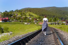 Young Woman Is Walking Along The Railway Tracks. Green Mountains In The Background