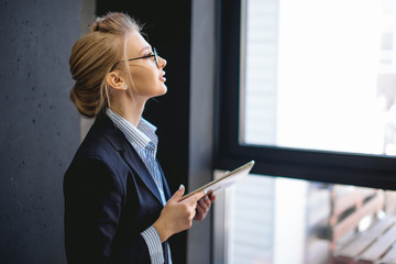 close up side view portrait of pleasant woman with fair hair holding her laptop and looking at the panorama window