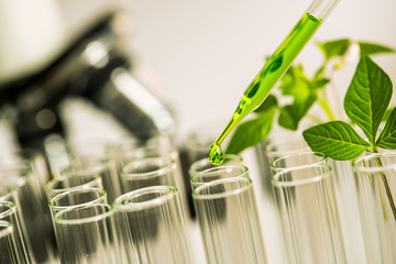 Poster - pipette over test tube dropping sample chemical into sample herbal plaint with microscope background , biotechnoloy research concept
