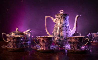 Food background tea and coffee theme. Old vintage ceramic tea or coffee pot with cups jug and sugar cup on dark background with lights and smoke. Silhouettes of ceramic tea pot and cup.