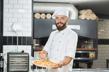 Smiling Bearded Pizzaiolo Holding Fresh Baked Mouthwatering Pizza.
