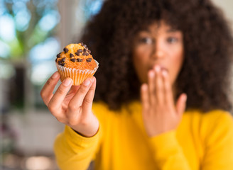 Poster - African american woman holding chocolate muffin cover mouth with hand shocked with shame for mistake, expression of fear, scared in silence, secret concept