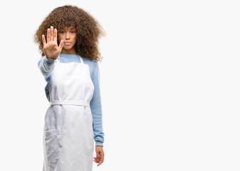 Poster - African american shop owner woman wearing an apron annoyed with bad attitude making stop sign with hand, saying no, expressing security, defense or restriction, maybe pushing