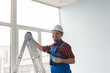 © satura_ - Happy male builder standing on ladder with screwdriver infront of window.