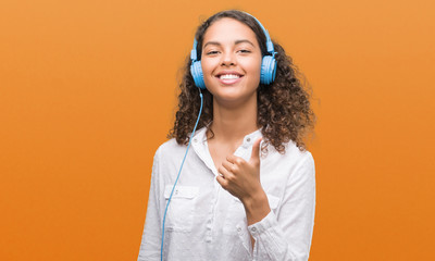 Young hispanic woman wearing headphones happy with big smile doing ok sign, thumb up with fingers, excellent sign