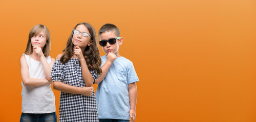 Wall Mural - Group of boy and girls kids over orange background serious face thinking about question, very confused idea