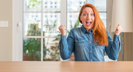 Sticker - Redhead woman at home celebrating surprised and amazed for success with arms raised and open eyes. Winner concept.