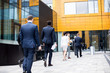 © pressmaster - Rear view of row of businesspeople in formalwear walking towards entrance of business center for conference