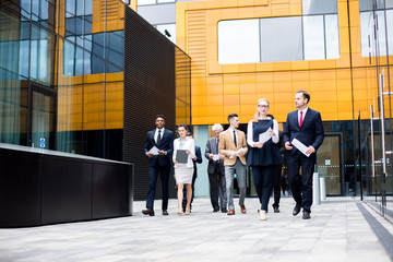 Wall Mural - Young intercultural businesspeople in suits came out for break between parts of conference in modern business center