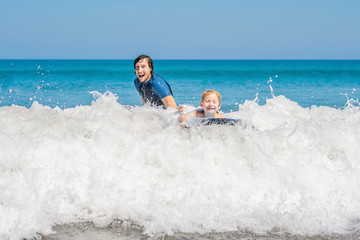 Father teaching his young son how to surf in the sea on vacation or holiday. Travel and sports with children concept