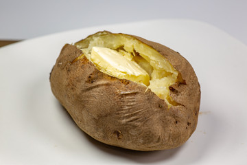 Fully loaded baked potato on a white plate on the kitchen table