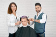 © serhiibobyk - Female and male hairstylists doing haircut for young client with toned hair. Using plastic combs for styling and sharp metallic scissors. Barber wearing waistcoat, woman having classic white shirt.