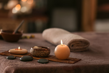 Wall Mural - Burning candles, stones and towel on massage table in spa salon