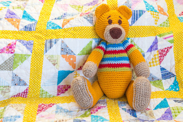 orange teddy bear sitting on colourful quilted duvet cover