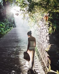 Young slim woman walking on old street in beautiful morning sun rays, amazing Bali nature and ancient architecture