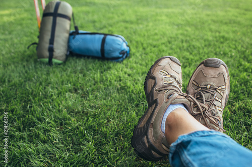 Fotografija Selfie of legs in trekking shoes on green grass near equipment for hiking and tr