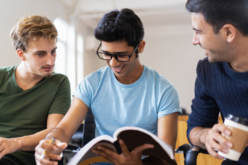 Three positive students studying together and drinking coffee. Young men sitting and socializing. Students concept. Front view.