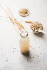 Canvas Print - Barley water in glass bottle with raw and cooked pearl barley wheat/seeds. selective focus