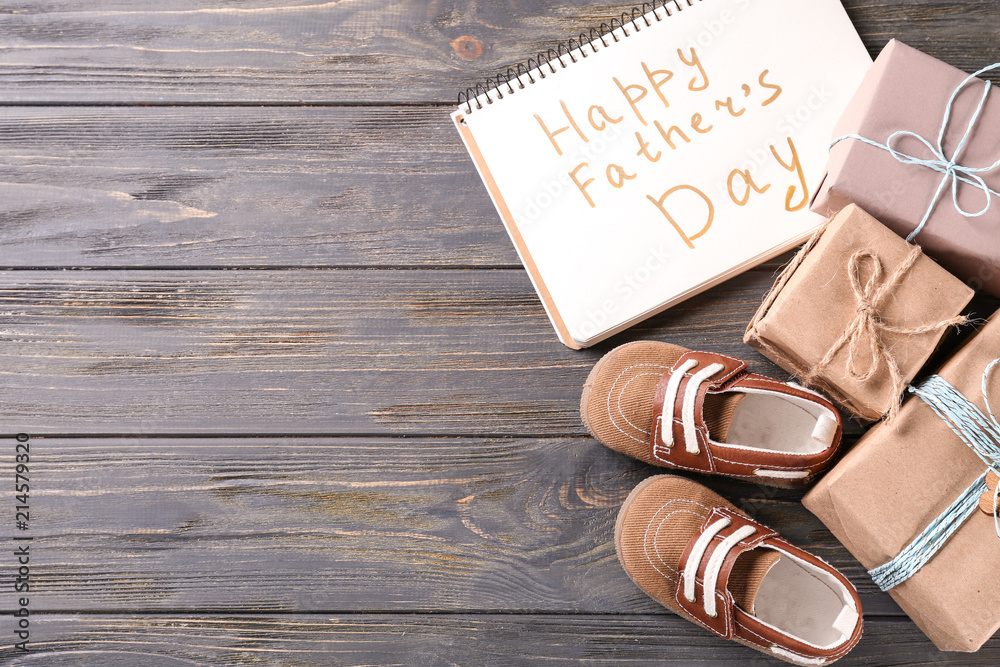 Composition with gift boxes, notebook and baby shoes on wooden background. Happy Father's day celebration