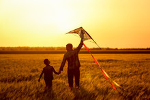 Happy Father And Son Flying Kite In The Field At Sunset