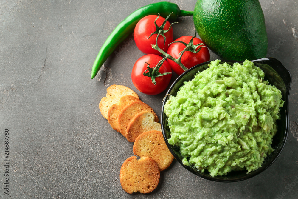 Tasty guacamole with bread chips and vegetables on grey textured background