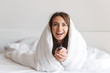 © Drobot Dean - Laughing young woman laying in bed covered in blanket