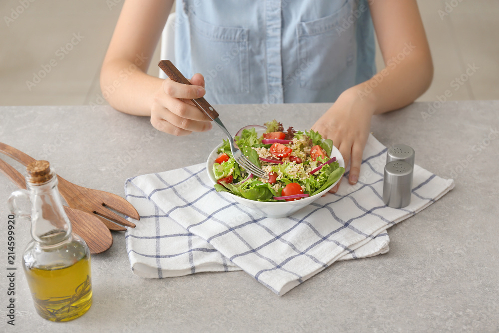 Woman eating tasty quinoa salad at table