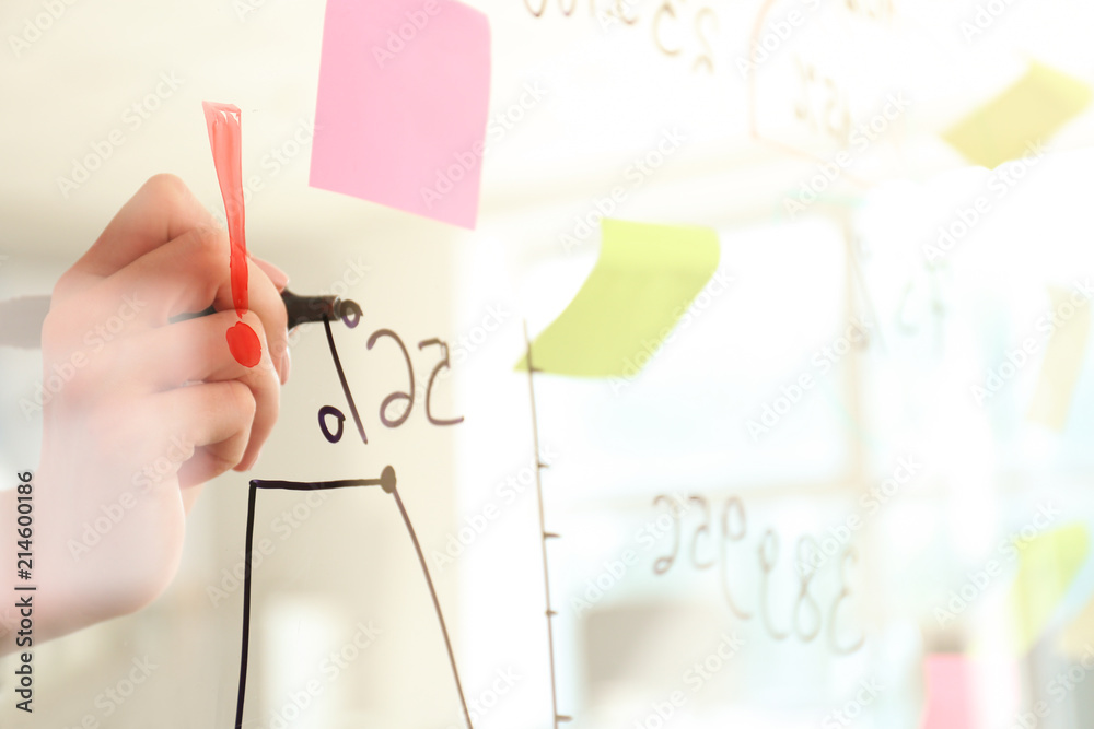 Woman writing on transparent board in conference hall, closeup