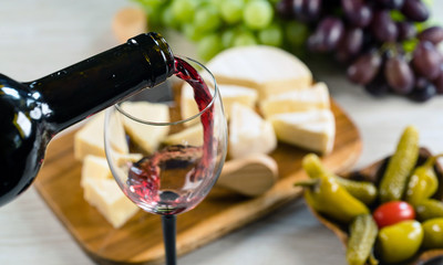  Pouring red wine into the glass in the background a table set with various types of cheese