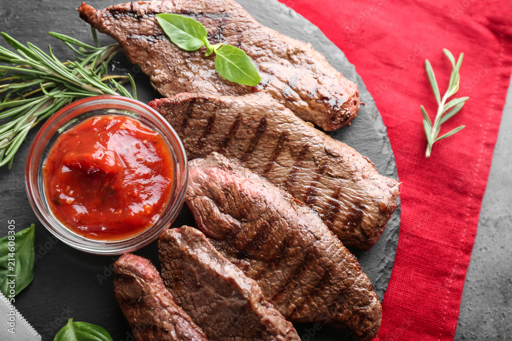 Tasty grilled meat with herbs and sauce on slate plate