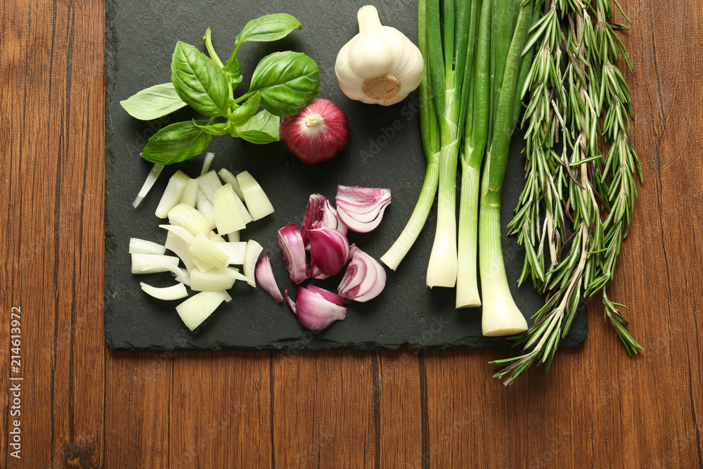 Slate plate with fresh onions, garlic and herbs on wooden table