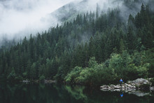 Foggy And Mystic Mountain Forrest With A Reflection On The Water And Person Standing In Front In Morskie Oko, High Tatras, Zakopane, Poland