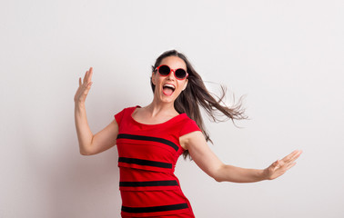 Wall Mural - A young beautiful delighted woman with red sunglasses and t-shirt in a studio.