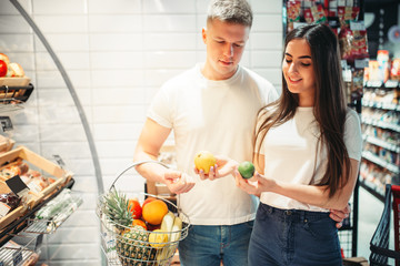 Wall Mural - Young couple choosing fresh fruits in supermarket