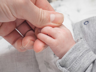 infant holding onto finger of adult male at closeup