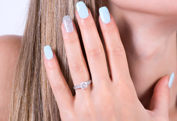 Beautiful girl with blue nails polish manicure and diamonds engagement wedding ring on finger. Female holding hand on hair and bare shoulders. Beauty and fashion concept. Close up, selective focus