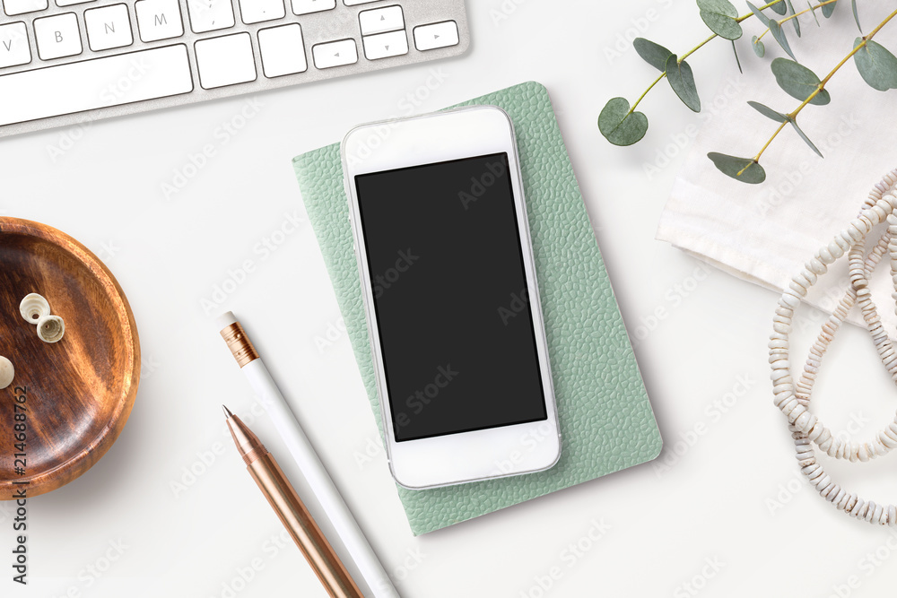 Bright feminine smartphone mockup with mint notebook, eucalyptus twigs, accessories and a wooden bowl on a white boho styled desk. Flat lay. - obrazy, fototapety, plakaty 