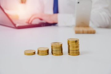 Golden coins on the table. There are gold coins on a white table, in the background a man, a businessman is working. Concept of financial growth, paying taxes, making money.