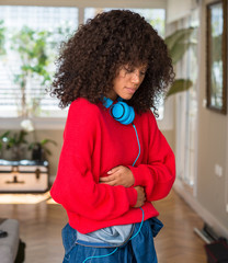 Poster - African american woman wearing headphones with hand on stomach because nausea, painful disease feeling unwell. Ache concept.