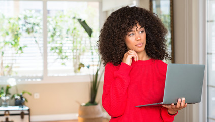 Poster - African american woman standing using computer laptop at home serious face thinking about question, very confused idea