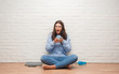 © Krakenimages.com - Young brunette woman sitting on the floor over white brick wall drinking coffee scared in shock with a surprise face, afraid and excited with fear expression
