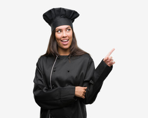 Sticker - Young hispanic cook woman wearing chef uniform very happy pointing with hand and finger to the side