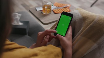 Slow motion hand woman using smartphone with green screen while sitting on the couch in the livinng room background tea many different spinning drugs technology chroma