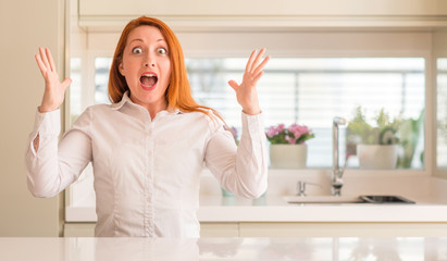 Sticker - Redhead woman at kitchen celebrating crazy and amazed for success with arms raised and open eyes screaming excited. Winner concept