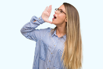 Canvas Print - Beautiful young woman wearing elegant shirt and glasses shouting and screaming loud to side with hand on mouth. Communication concept.