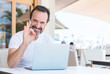 © Krakenimages.com - Handsome senior man using laptop at restaurant doing ok sign with fingers, excellent symbol