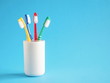 four colored toothbrushes in a glass on a light blue background 