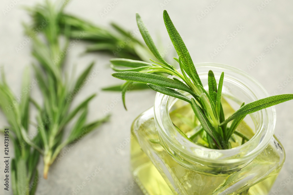 Glass jar with oil and fresh rosemary on grey background